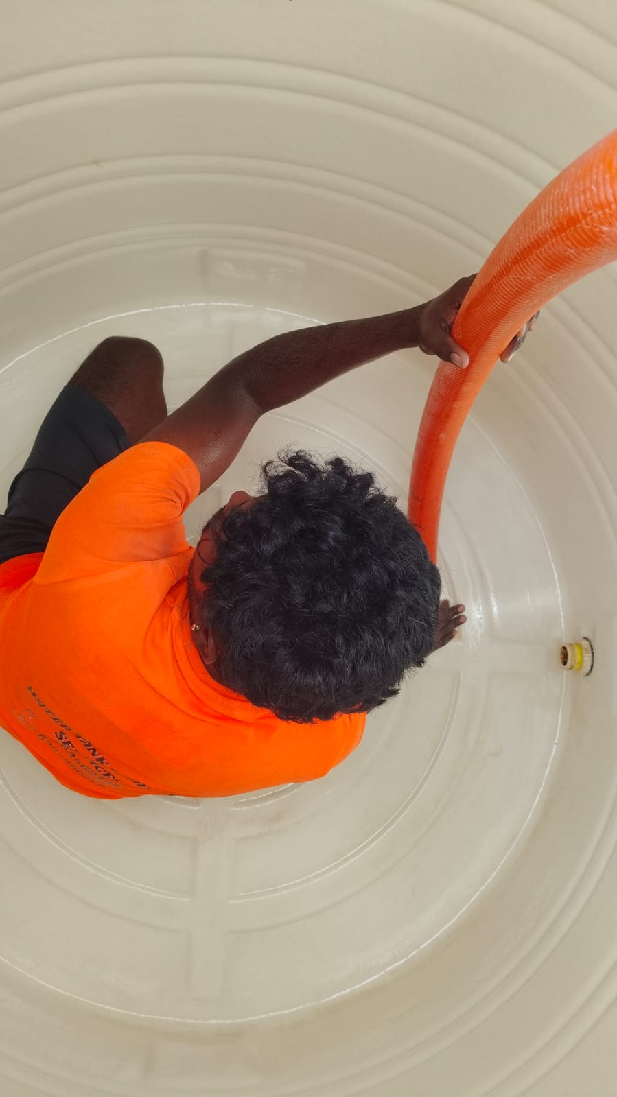 Technician dewatering a cleaned white water tank with a large orange suction hose